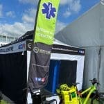 Event Medical Cover 4 Outdoor medical centre tent with a prominent green flag featuring a white medical symbol. A yellow bicycle with medical equipment is parked nearby.