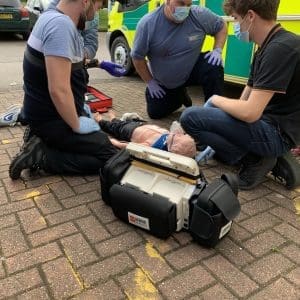 Three people treating a mannequin outdoors near an ambulance. They're wearing masks and gloves, concentrating intently on our Level 3 Certificate in First Response Emergency Care FREC 3 course. First Response Emergency Care (FREC 3)